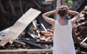 A woman stands with her heads on her hands in front of her burned home.