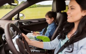 A photo of a mother driving in the car with her daughter who is looking at a  smartphone
