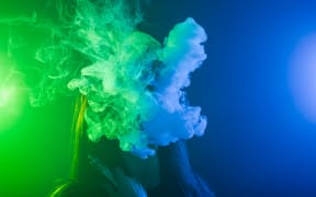 Portrait of asian woman smoking vape or e-cigarette in neon light at black background