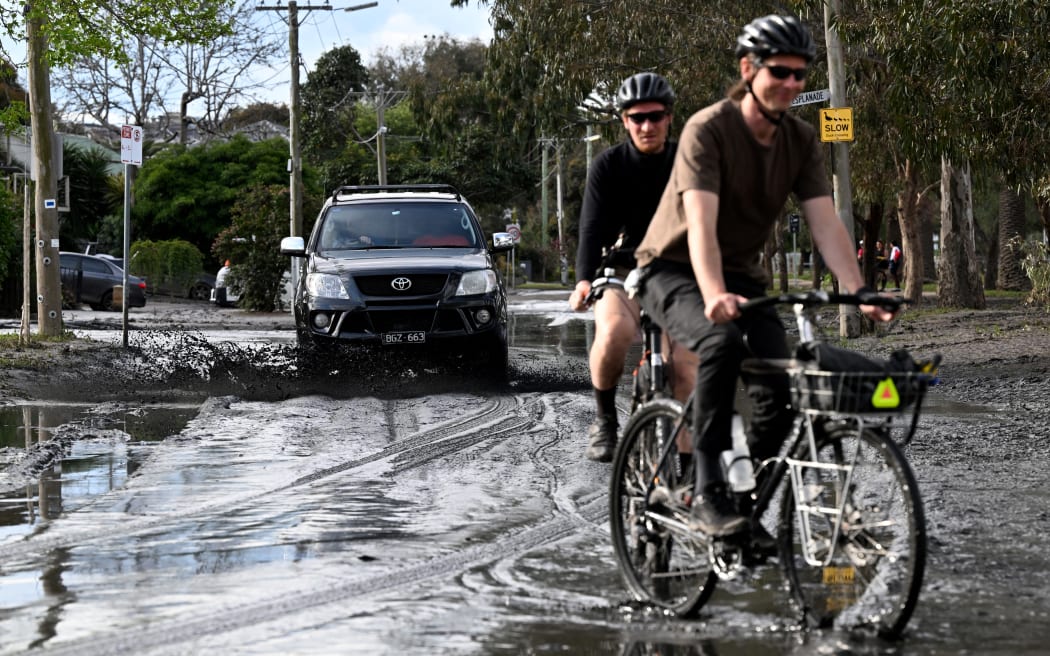 15 Ekim 2022'de Melbourne banliyösü Maribyrnong'da insanlar selden zarar görmüş çamurlu sokaklarda bisiklet ve araba kullanıyorlar. - Avustralya, şiddetli yağmurların düşmesine ve sel seviyelerinin aşılmasına rağmen 15 Ekim 2022'de günler süren yaygın sel nedeniyle ilk ölümünü bildirdi .  güneydoğunun büyük bir bölümünde.  Yüzlerce ev sahibi, yağmur suyunun üç eyalette sokakları, evleri ve arabaları süpürmesinin ardından uzun bir temizlik başlattı ve Melbourne banliyöleri en kötü etkilenenler arasında.  (Fotoğraf: William West/AFP)