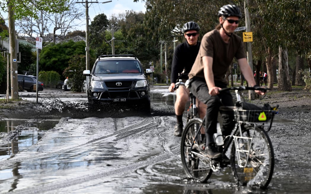 Ludzie jeżdżą rowerami i samochodami przez błotniste ulice zniszczone przez powódź na przedmieściach Melbourne w Maribyrnong 15 października 2022 r. - Australia zgłosiła swoją pierwszą śmierć w wyniku dni powszechnych powodzi 15 października 2022 r., chociaż spadły ulewne deszcze i poziom powodzi przekroczył .  przez większą część południowego wschodu.  Setki właścicieli domów rozpoczęło długotrwałe sprzątanie po tym, jak woda deszczowa zalała ulice, domy i samochody w trzech stanach, a przedmieścia Melbourne były najbardziej dotknięte.  (Zdjęcie: William West/AFP)