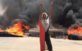 A protester in front of burning tires and debris on the road near Khartoum's army headquarters.