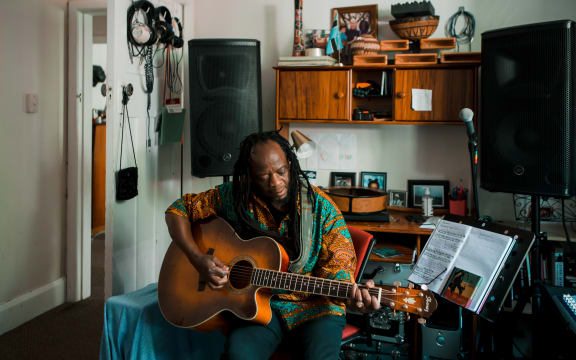 Judah Seomeng playing guitar in his house in Te Whanganui-a-Tara