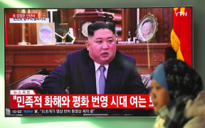 A woman walks past a television news screen showing a New Year speech by North Korean leader Kim Jong Un.