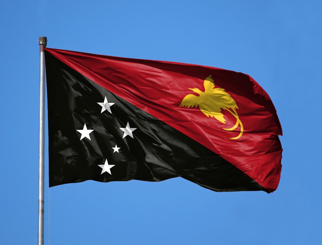 National flag of Papua New Guinea on a flagpole in front of blue sky.