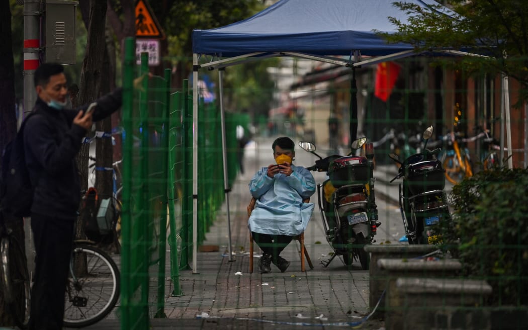 A guard is seen through a fence closing an area in lockdown in the Changning district, after new Covid-19 cases were reported in Shanghai, on October 8, 2022. (Photo by Hector RETAMAL / AFP)