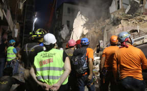 Lebanese and Chilean rescue workers watch as a crane lifts pieces of cement from a badly damaged building in Lebanon's capital Beirut, in search of possible survivors