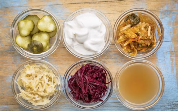 a set of fermented food great for gut health - top view of glass bowls against grunge wood:  cucumber pickles,  coconut milk yogurt, kimchi, sauerkraut, red beets, apple cider vinegar