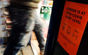 A man passes a notice warning of the current 'high' alert level for covid-19, taped at the entrance to a newsagent on Old Compton Street in Soho in London, England