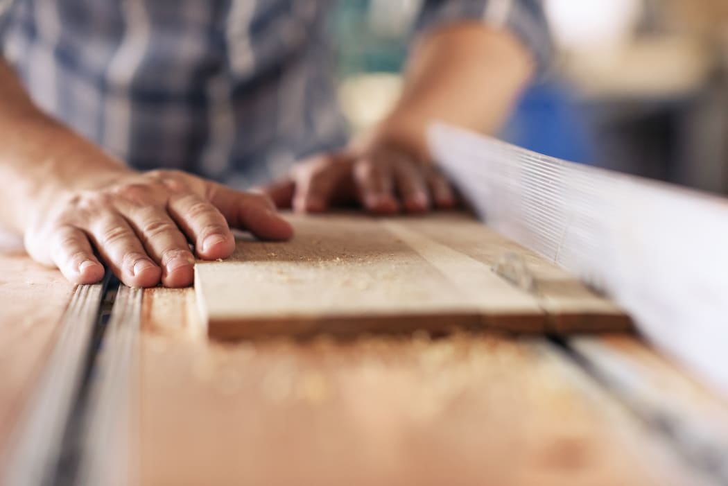Closeup of a skilled carpenter sawing a piece of wood with a table saw while working alone in his woodworking studio