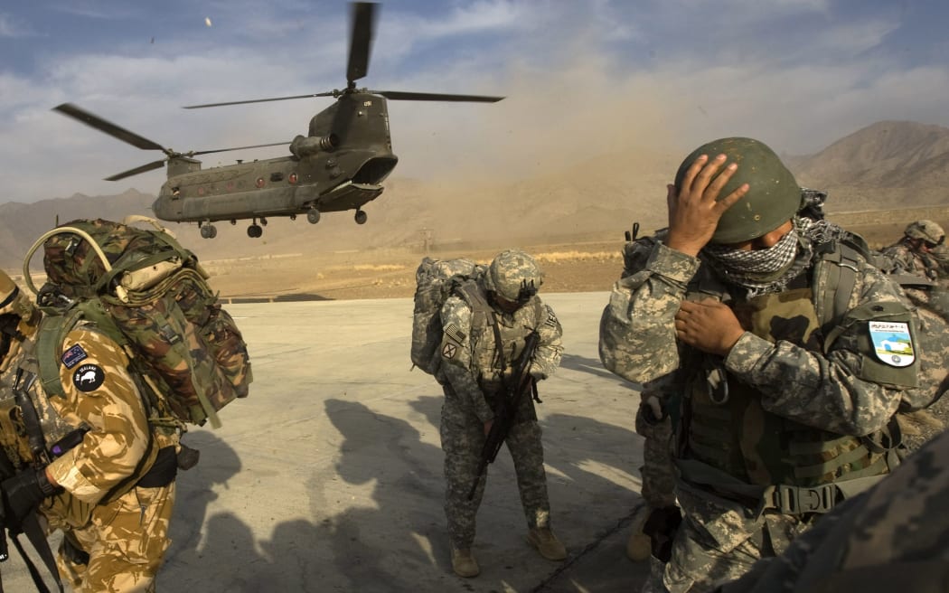 US Army soldiers from 2-506 Infantry 101st Airborne Division, Afghan National Army soldiers and a New Zealand Army soldier take cover as a CH-47 Chinook helicopter lands to transport them nto the Spira mountains in Khost province, in November 2008.  AFP PHOTO/DAVID FURST (Photo by DAVID FURST / AFP)