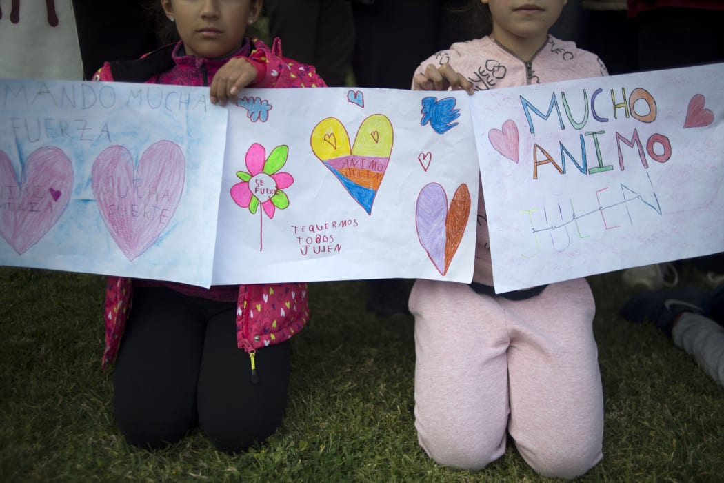 Two girls hold drawings bearing hearts and messages of support as rescue workers continue efforts to find a boy who fell down a well in Totalan in southern Spain on January 16, 2019.