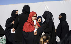 Displaced Iraqi women who fled the violence in the Islamic State group stronghold of Mosul, gather for food near the town of Bartella on 14 January, 2017, during a military operation by Iraqi security forces against IS fighters.