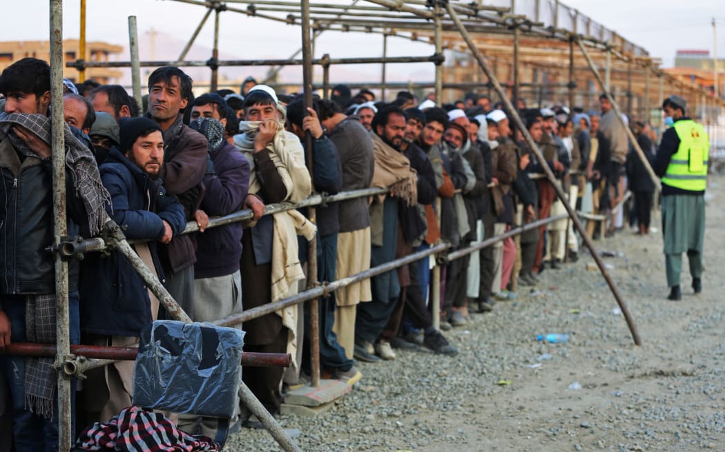 Afghan men stand in queues to receive food aid from a non-governmental organisation (NGO) in Kabul on December 25, 2022.