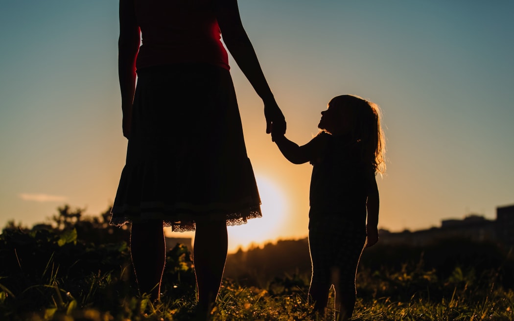 silhouette of mother and daughter holding hands in nature at sunset