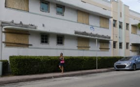 A woman walks by a building with boarded up windows during a hurricane alert for this weekend in South Miami Beach, Florida.