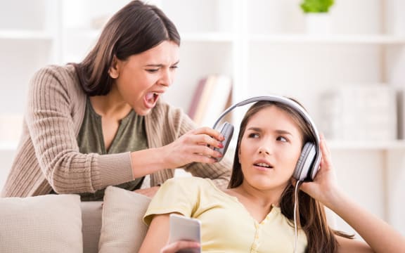 A photo of a mother pulling headphones off her teenage daughterwho is not listening to her