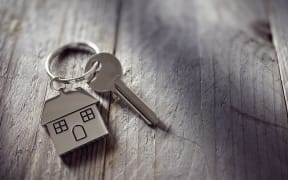 House key on a house shaped keychain resting on wooden floorboards concept for real estate, moving home or renting property
