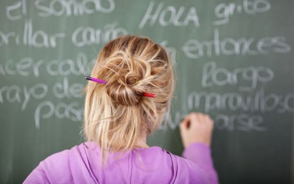 Student writing Spanish words on blackboard (stock photo).