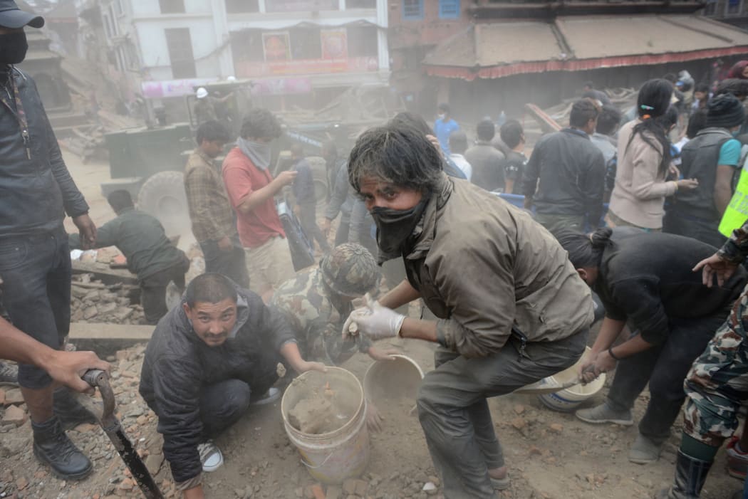 People work to clear rubble in Durbar Square, surrounded by dust.