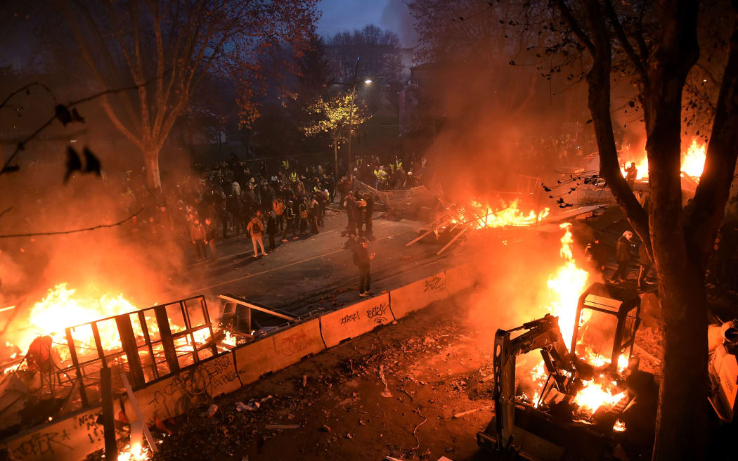 Protestors wearing a yellow vest (gilet jaune) stand next to a burning barricade, during a demonstration against rising costs of living they blame on high taxes in Toulouse, southern France