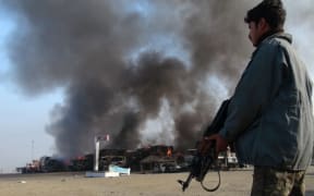Afghan security personnel stand alert near burning NATO military vehicles after a clash between Taliban and Afghan security forces in 2013.