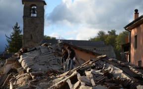Two men walk on a damaged home after a strong heartquake hit Amatrice