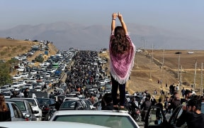 This UGC image posted on Twitter reportedly on October 26, 2022 shows an unveiled woman standing on top of a vehicle as thousands make their way towards Aichi cemetery in Saqez, Mahsa Amini's home town in the western Iranian province of Kurdistan, to mark 40 days since her death, defying heightened security measures as part of a bloody crackdown on women-led protests. - A wave of unrest has rocked Iran since 22-year-old Amini died on September 16 following her arrest by the morality police in Tehran for allegedly breaching the country's strict rules on hijab headscarves and modest clothing. (Photo by UGC / AFP) / === RESTRICTED TO EDITORIAL USE - MANDATORY CREDIT "AFP PHOTO / UGC IMAGE" - NO MARKETING NO ADVERTISING CAMPAIGNS - DISTRIBUTED AS A SERVICE TO CLIENTS FROM ALTERNATIVE SOURCES, AFP IS NOT RESPONSIBLE FOR ANY DIGITAL ALTERATIONS TO THE PICTURE'S EDITORIAL CONTENT, DATE AND...