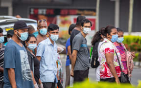This picture taken on April 24, 2021 shows residents wearing face masks waiting to cross the main road in the Fijian capital Suva ahead of an expected lockdown in the capital due to a Covid-19 spike. (Photo by Leon LORD / AFP)