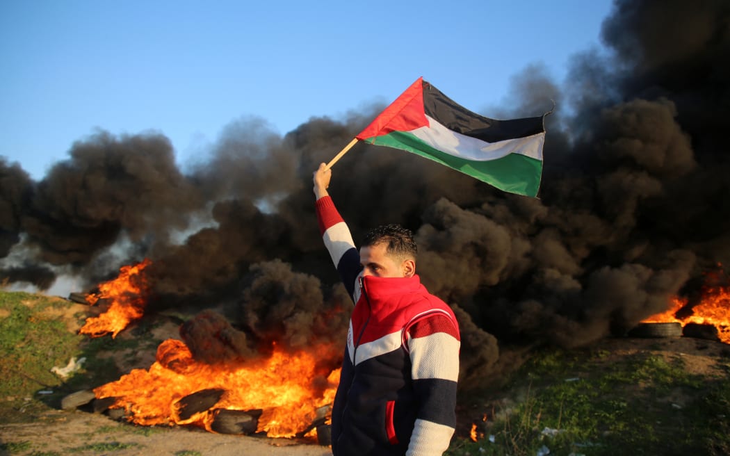 A Palestinian man holds a Palestinian flag during clashes with Israeli forces, near the Israel-Gaza border east of Gaza City, January 26, 2023.
