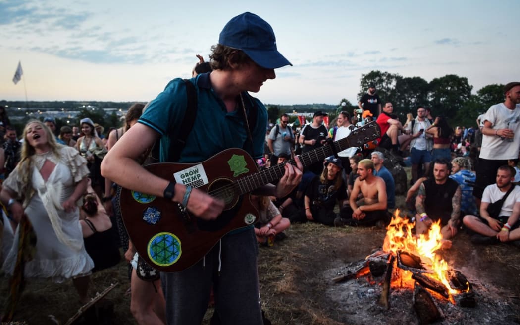 A festivalgoer plays the guitar around a bonfire during the Glastonbury festival near the village of Pilton in Somerset, southwest England, on June 22, 2022. - More than 200,000 music fans and megastars Paul McCartney, Billie Eilish and Kendrick Lamar descend on the English countryside this week as Glastonbury Festival returns after a three-year hiatus. The coronavirus pandemic forced organisers to cancel the last two years' events, and those going this year face an arduous journey battling three days of major rail strikes across the country. (Photo by Andy Buchanan / AFP)