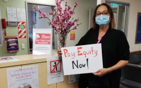 In an image supplied by the PSA, a District Health Board clerical worker holds a sign reading 'pay equity now'.