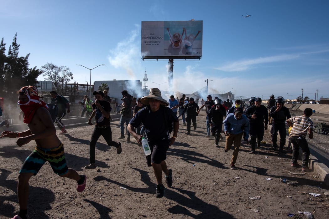 Central American migrants - mostly Hondurans - run along the Tijuana River near the El Chaparral border crossing in Tijuan, after the US border patrol threw tear gas from the distance to disperse them.