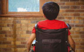 Rear view of little boy sitting in wheelchair in school