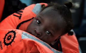 child from African origin looks on as she is rescued from a distressed vessel by a member of Proactiva Open Arms NGO in the mediteranean sea some 20 nautical miles north of Libya on October 3, 2016.
