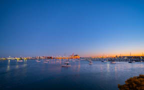 lights of Port of Tauranga ships and harbor at dawn with golden glow of sun on horizon.