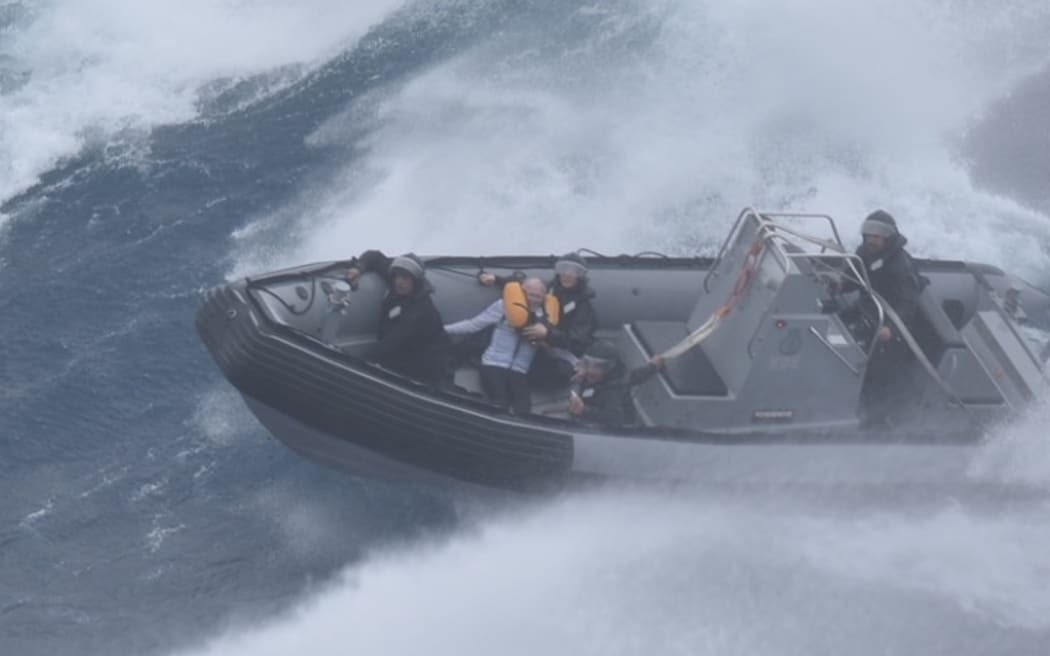 Members of the navy take a man to safety in an inflatable hull vessel after his catamaran drifted out to sea in strong winds.