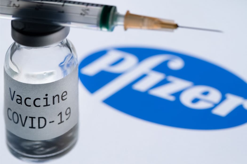 File: This illustration picture taken in Paris on November 23, 2020 shows a syringe and a bottle reading "Covid-19 Vaccine" next to the Pfizer company logo.