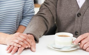 Close Up Of Woman Sharing Cup Of Tea With Elderly Parent