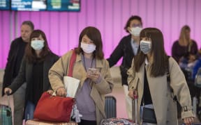 Passengers wear protective masks to protect against the spread of the Coronavirus as they arrive at the Los Angeles International Airport.