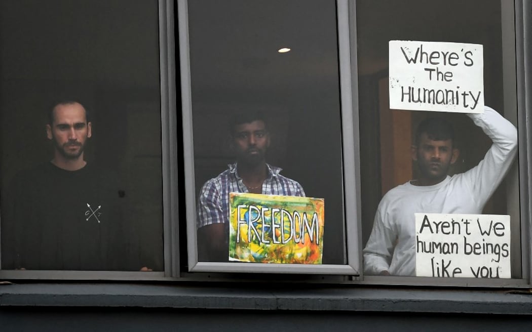 Three asylum seekers gesture to protesters holding a pro-refugee rights rally from their hotel room where they have been detained in Melbourne on June 13, 2020, after they were evacuated to Australia for medical reasons from offshore detention centres on Nauru and Manus Island.