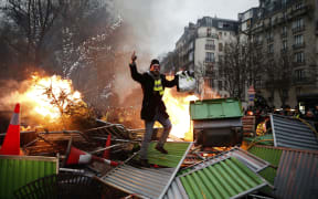 A demonstrator gestures on a burning barricade on January 5, 2019 in Paris, during an anti-government demonstration called by the yellow vest "Gilets Jaunes" movement.