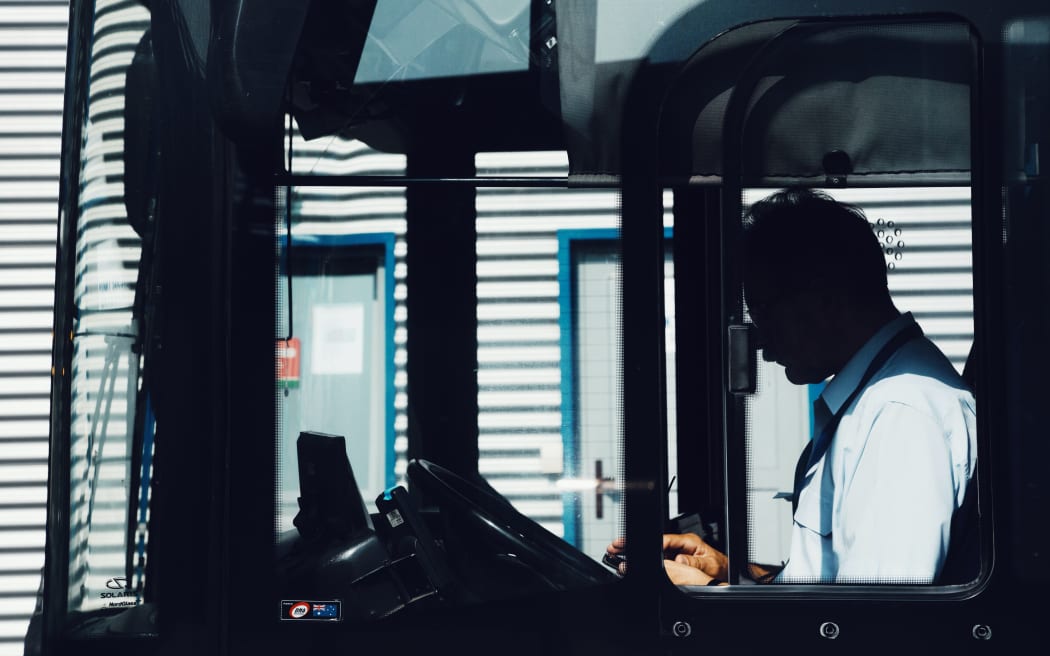 A person sitting in the drivers seat of a bus.