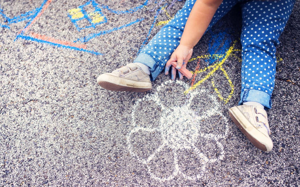 Close up of little girl in canvas shoes drawing with chalks on the sidewalk.