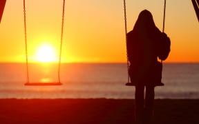 Back view portrait of a single woman silhouette sitting on a swing contemplating sunset