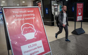 A man, not wearing a face covering, passes signs telling travellers they must wear face mask unless they are exempt, as he leaves Victoria station during the evening 'rush hour' in central London on September 23, 2020. -
