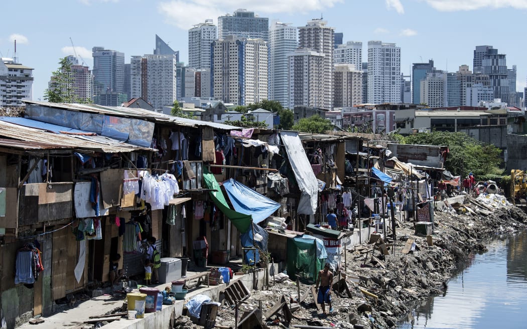 People living in a settlement walk about, as the skyline of Manila's financial district is seen in the background, on August 17, 2017.