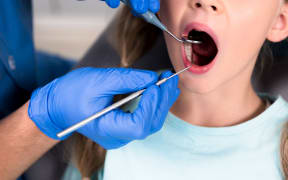 cropped shot of dentist with instruments examining teeth of little child