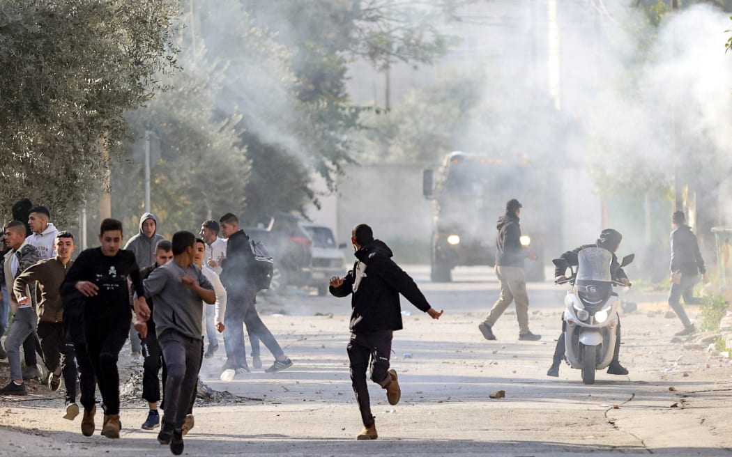 Palestinians run for cover during confrontations with Israeli forces in the occupied-West Bank city of Jenin, on January 26, 2023. - An Israeli raid on the West Bank's Jenin refugee camp today killed nine Palestinians including an elderly woman, Palestinian officials said.