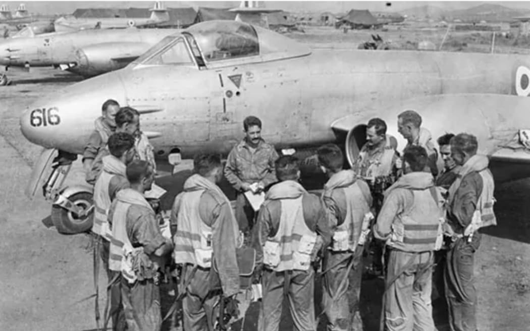 Pilots of No.77 Squadron  RAAF, being briefed by their Commanding Officer, Squadron Leader Dick Cresswell (centre, facing camera), on the Kimpo airfield tarmac in front of a Meteor aircraft, prior to a mission over North Korea in 1951. Flight Lieutenant Max Scannell, RAF is second  from the left in the semicircle.